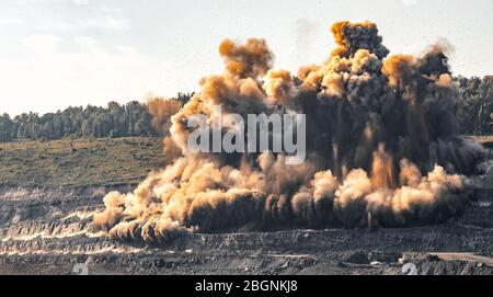 Des engins explosifs sont à ciel ouvert dans l'industrie des mines de charbon. Poussière et bouffées de fumée dans le ciel, sol sablé Banque D'Images