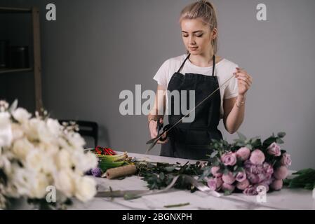 Jeune fleuriste séduisant portant un tablier de coupe corde pour envelopper le bouquet de fleurs Banque D'Images