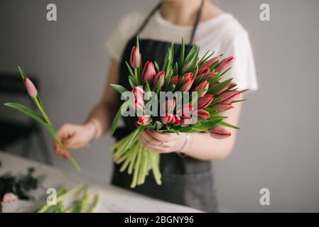 Jeune fleuriste méconnaissable portant un tablier, faisant de la composition florale de roses fraîches à la table Banque D'Images