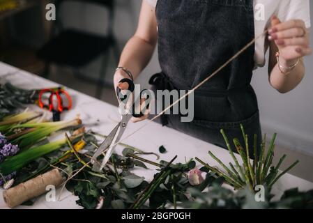 Gros plan des mains de femme fleuriste coulant corde pour envelopper bouquet de fleurs à la table Banque D'Images