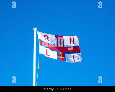 Un drapeau RLI légèrement déchiqueté flutters dans le vent à Amble, Northumberland. Banque D'Images