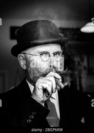 Portrait monochrome en gros plan de l'homme britannique des années 1940 avec moustache en guidon et chapeau melon fumant cigare, événement d'été des années 1940 au Royaume-Uni. Banque D'Images