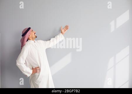 Un homme arabe heureux en vêtements blancs montre une présentation sur fond de main Banque D'Images