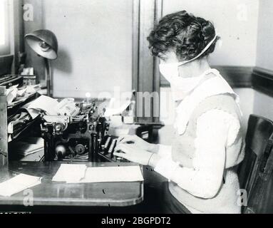Une dactylographe féminine portant un masque au travail pendant l'épidémie de grippe de 1918-1919. Banque D'Images