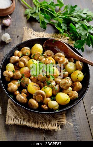 Champignons frits avec pommes de terre dans une poêle en fonte sur table en bois Banque D'Images