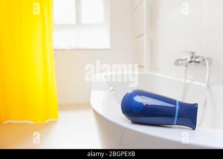 Sèche-cheveux allongé sur une baignoire dans une salle de bains lumineuse - danger de choc électrique - foyer sélectif sur le sèche-cheveux Banque D'Images