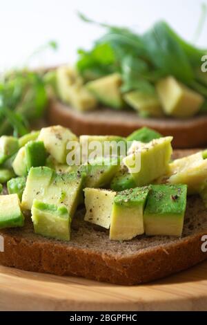 Petit déjeuner sain pain de seigle grillé avec avocat, rugula, jus de citron, sel et poivre sur une plaque en bois Banque D'Images