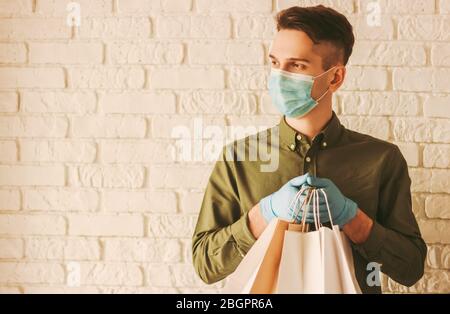 Courrier pour jeunes hipster dans un masque de protection, gants médicaux contenant des sacs à provisions dans les mains. Liveur avec paquets de papier. Livraison en ligne sécurisée s Banque D'Images