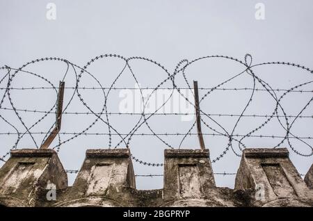 Fil concertina placé sur le dessus d'un mur. Ciel gris nuageux Banque D'Images