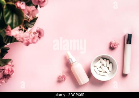 Bouteilles cosmétiques et capsules blanches avec fleurs de mensonia sur fond de papier rose. Concept de santé et de beauté. Banque D'Images