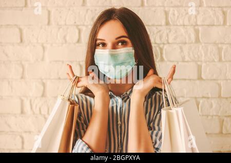 Belle fille cabas dans le masque de visage médical tenant des sacs de shopping dans les mains. Jeune femme heureuse client dans le masque de protection sur le visage avec des sacs en papier. RIF Banque D'Images