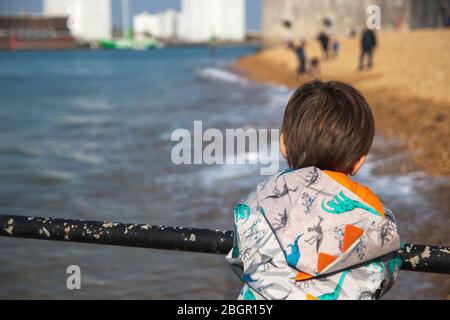 Un petit garçon debout seul regardant sur les rampes au bord de la mer Banque D'Images