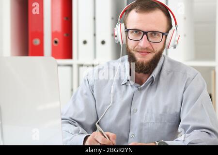 Un homme en casque d'écoute de la musique et apprend en ligne. Prend des notes sur un ordinateur portable et s'intéresse à l'appareil photo Banque D'Images