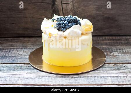 Gâteau jaune à la vanille et au citron avec meringues et raisins frais, bleuets, mûres. Fond rustique en bois. Banque D'Images