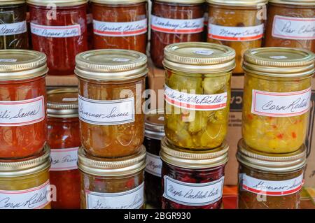 Des bocaux empilés colorés de confitures maison, de gelées, de chutneys et d'autres conserves remplissent une table sur le marché d'un agriculteur local. Banque D'Images