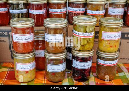 Des bocaux empilés colorés de confitures maison, de gelées, de chutneys et d'autres conserves remplissent une table sur le marché d'un agriculteur local. Banque D'Images