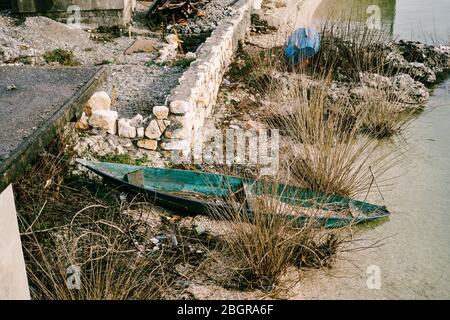 Un bateau inondé de bois sur la rive de la rivière entre les buissons et les débris sur la rive Banque D'Images