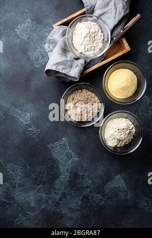 Divers légumes farine sans gluten maïs, sésame, avoine, noix de coco dans un bol en verre sur fond gris foncé.alternative à la farine de blé pour le régime de keto paleo Banque D'Images