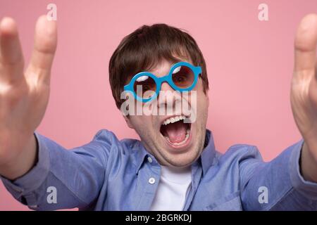 Selfie funky au téléphone. Le jeune homme caucasien prend des verres d'été sur le dos rose, étonné, extrêmement heureux Banque D'Images