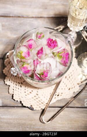 Glaçons avec fleurs roses dans un seau en verre et deux verres avec champagne sur fond de table en bois Banque D'Images