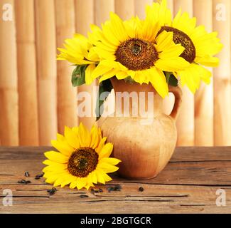 Beau bouquet de tournesols dans le pichet sur la table sur fond en bois Banque D'Images