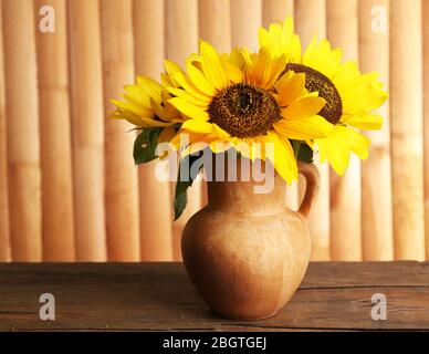 Beau bouquet de tournesols dans le pichet sur la table sur fond en bois Banque D'Images