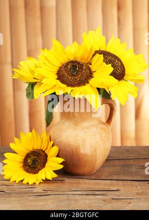 Beau bouquet de tournesols dans le pichet sur la table sur fond en bois Banque D'Images