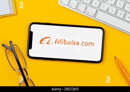 Un smartphone affichant le logo Alibaba repose sur un fond jaune avec un clavier, des lunettes, un stylo et un livre (usage éditorial uniquement). Banque D'Images