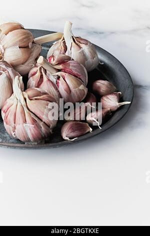 Une pile d'ail violet sur une plaque rustique sur un fond de marbre. Concept de nourriture et de condiment. Banque D'Images