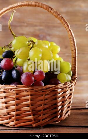 Différents types de raisins dans le panier en osier sur fond en bois Banque D'Images