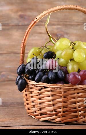 Différents types de raisins dans le panier en osier sur fond en bois Banque D'Images