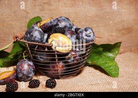 Prunes douces mûres dans le vieux panier en métal, sur table en bois Banque D'Images