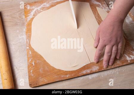 Les mains femelles tranchez la pâte sur un tableau de découpe avec un couteau blanc. Cuisine à la maison. Banque D'Images