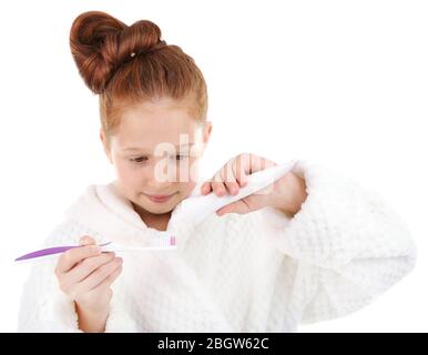 Belle petite fille dans peignoir tenant brosse à dents et dentifrice isolé sur blanc Banque D'Images