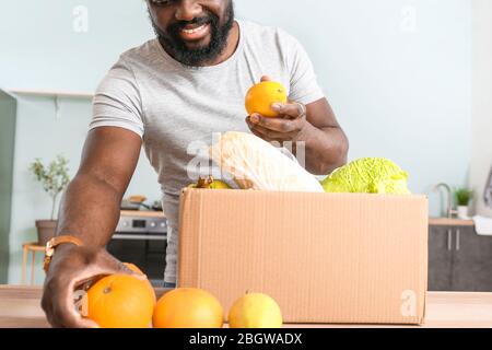 Homme afro-américain qui dédéballage des produits frais du marché en cuisine Banque D'Images