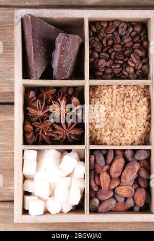 Boîte en bois avec ensemble de grains de café et de cacao, de cubes de sucre, de chocolat noir, de cannelle et d'anis sur fond de bois Banque D'Images