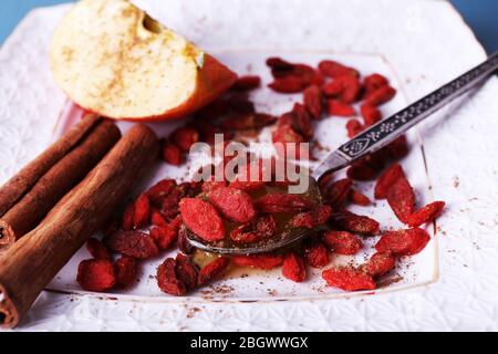 Pomme mûre, miel en cuillère, baies de goji et cannelle sur la plaque carrée blanche sur la fermeture Banque D'Images