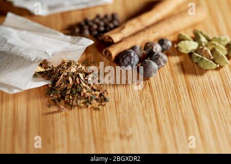 Gros plan sur un sachet de thé ouvert aux herbes, aux baies de genévrier et aux herbes, aux bâtonnets de cannelle, aux épices et au cardamon sur un plateau de découpe en bambou peu profond Banque D'Images