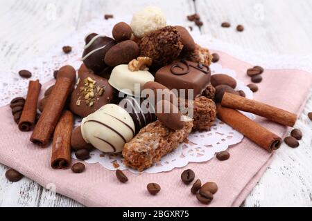 Tas de chocolats doux avec des grains de café sur des matériaux roses et des miily blanches sur fond de bois Banque D'Images