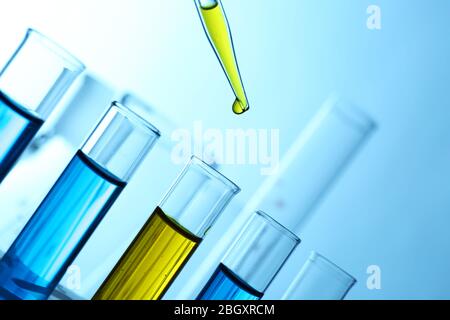 Pipette ajoutant du liquide jaune à l'un des plusieurs tubes à essai avec flacons sur fond clair Banque D'Images