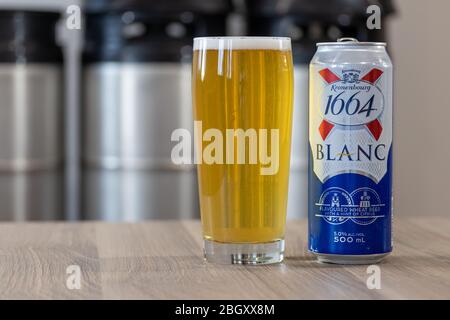 Kronenbourg 1664 Blanc bière peut sur une table à côté d'un verre de bière avec des kegs empilés en arrière-plan Banque D'Images