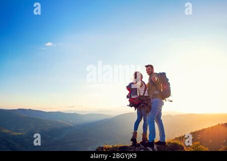 heureux couple homme et femme touriste au sommet de la montagne au coucher du soleil dehors pendant une randonnée en été Banque D'Images