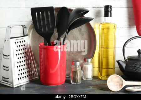 Ustensiles de cuisine en plastique dans une tasse rouge avec bouteille d'huile d'olive sur fond en bois Banque D'Images