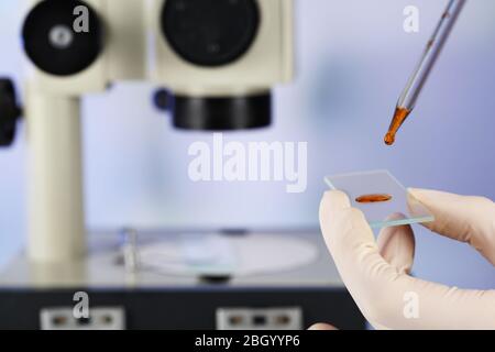 Main assistant dans des gants pour faire des analyses en laboratoire au microscope et sur fond flou Banque D'Images
