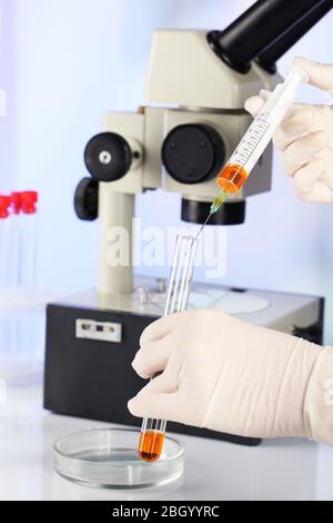 Assistant mains dans des gants pour faire des analyses en laboratoire avec microscope et fond flou Banque D'Images