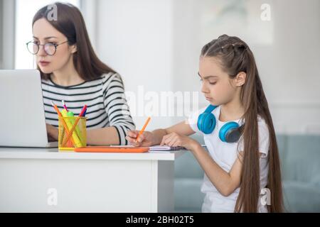 Jeune femme dans des verres et fille avec casque assis à la table. Banque D'Images