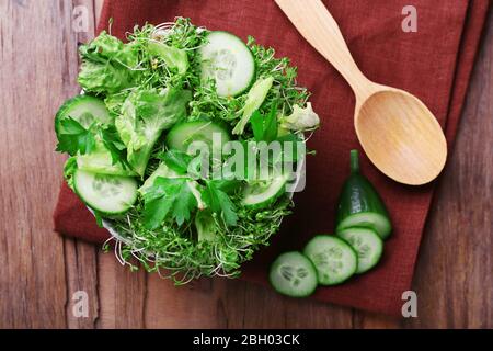 Salade de cresson avec concombre en tranches et persil dans un bol en verre sur fond rustique de table en bois Banque D'Images