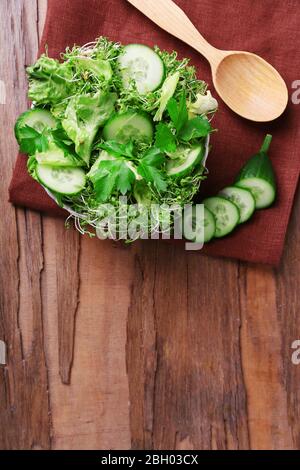 Salade de cresson avec concombre en tranches et persil dans un bol en verre sur fond rustique de table en bois Banque D'Images