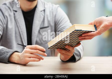 Auteur signe autographe dans son propre livre à une table en bois sur fond flou léger Banque D'Images