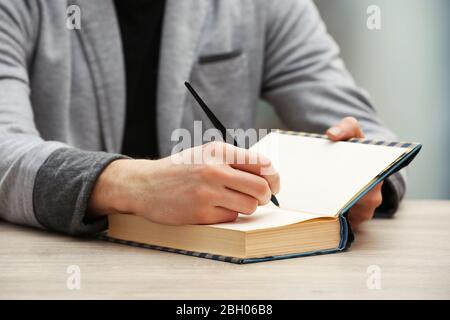 Auteur signe autographe dans son propre livre à une table en bois sur fond flou léger Banque D'Images